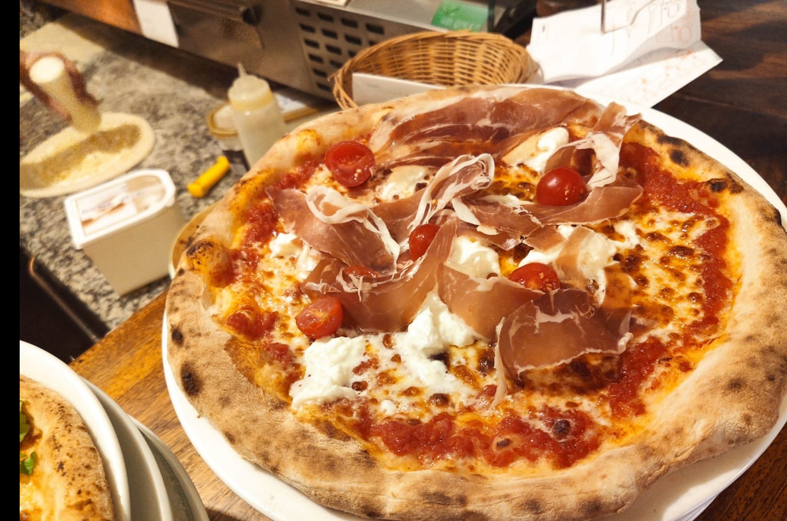 Pizza au jambon de Parme, burrata et tomates cerises, cuite au feu de bois